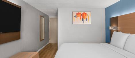 Habitación de hotel con cama, televisor de pantalla plana, cómoda de madera y una obra de arte colgada en la pared.