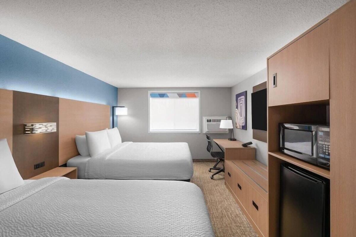 Een hotelkamer met twee bedden, een bureau met een computer, een magnetron en een koelkast.