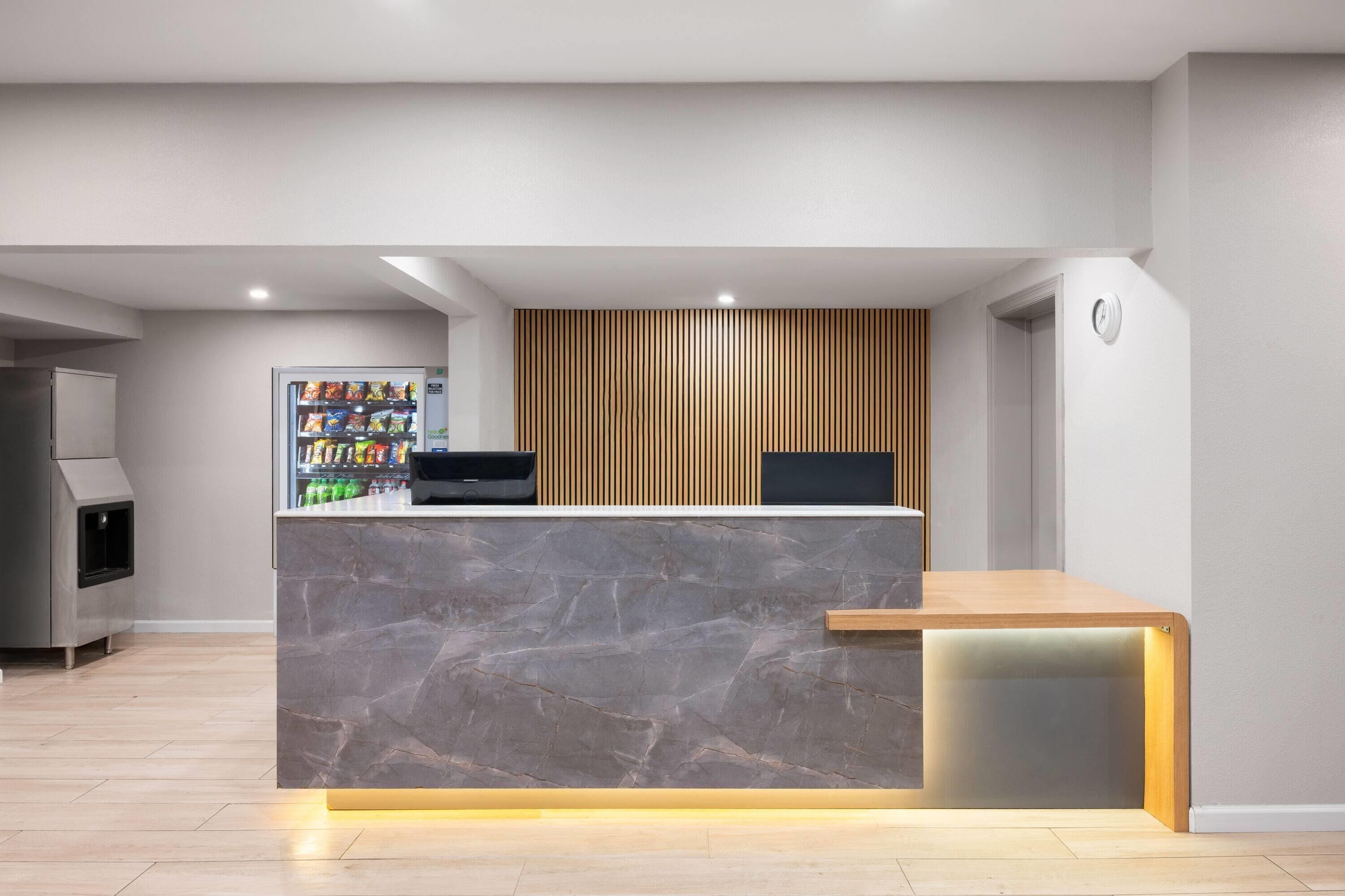 A reception desk with a marble top, a vending machine, and a wooden slat wall.