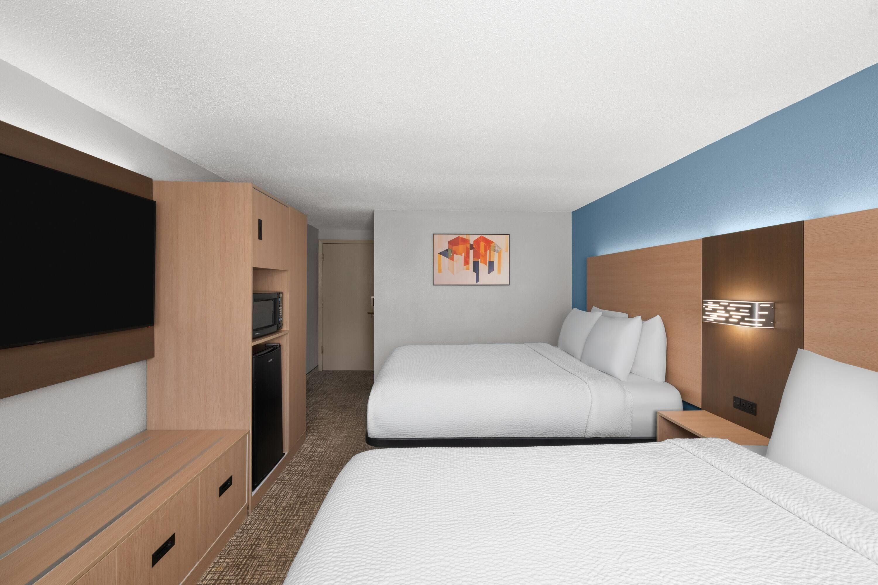 Habitación de hotel con dos camas, televisión de pantalla plana, microondas y un cuadro en la pared.