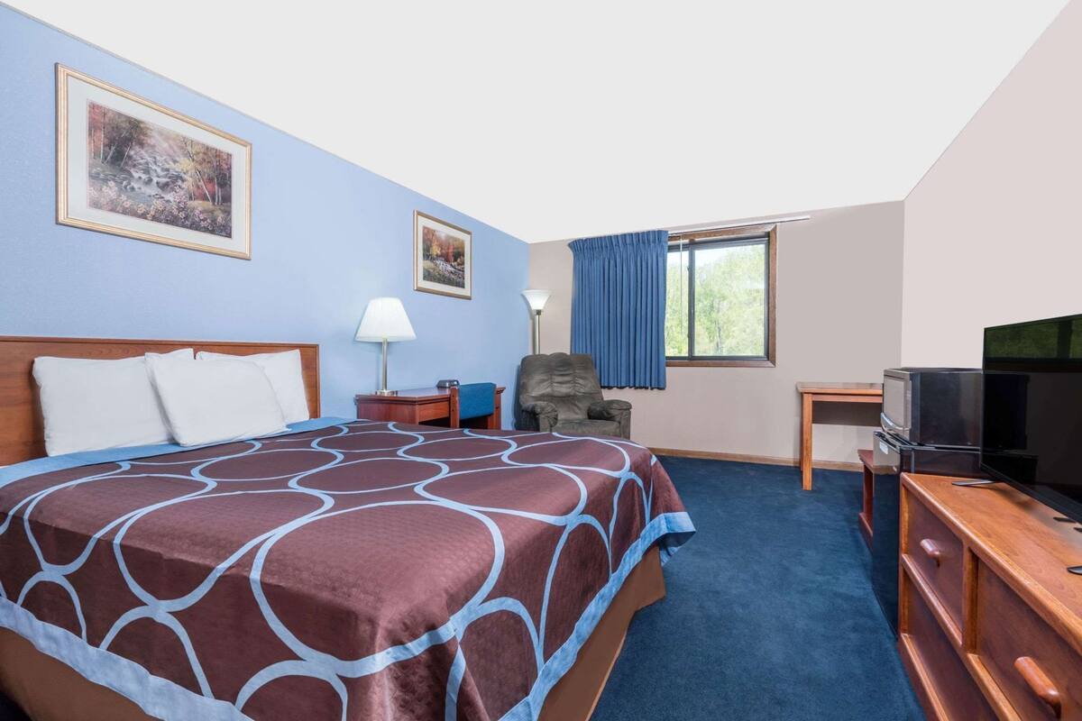 Een hotelkamer met een groot bed, een bureau, een stoel, een televisie en twee foto's in lijsten aan de muur.