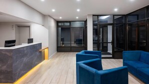 Un área de recepción moderna con una encimera de mármol, asientos azules y puertas de vidrio que dan a un balcón.