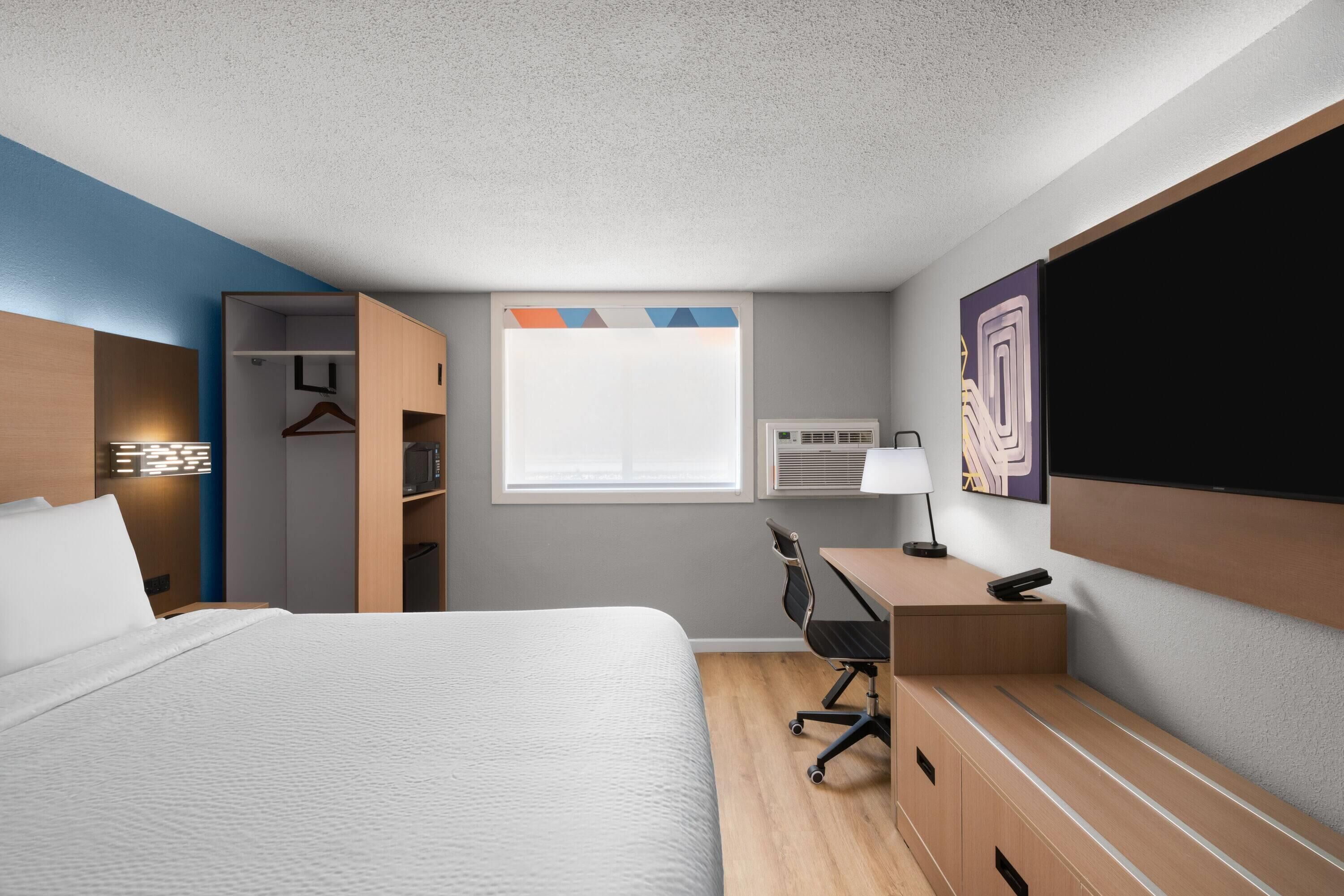 Habitación de hotel con cama, escritorio, silla, armario y un ventanal grande.