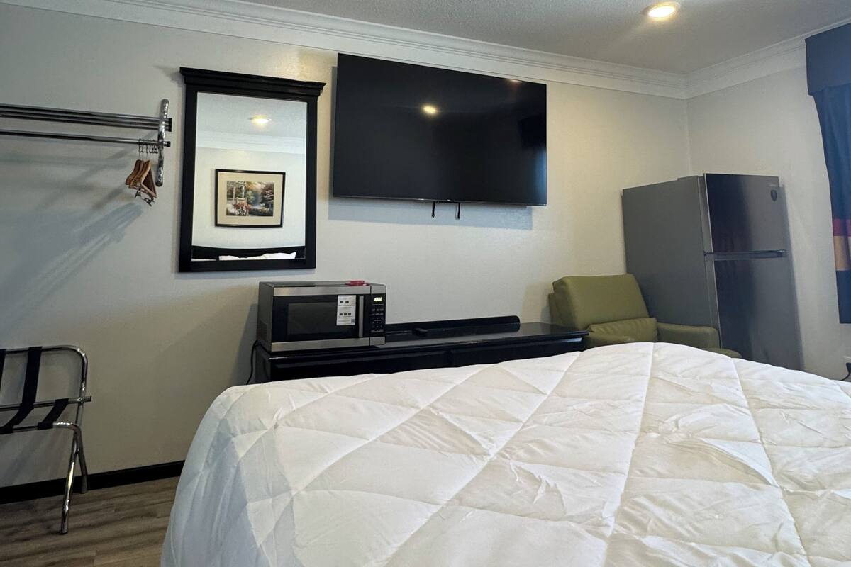Ein Hotelzimmer mit einem großen Bett, einem flachbildfernseher an der Wand, einer Mikrowelle, einem Kühlschrank und einer Sitzecke mit einem Sessel und einem kleinen Tisch.