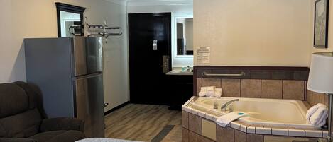 A hotel room with a bed, a kitchenette, a bathroom with a bathtub, and a seating area.