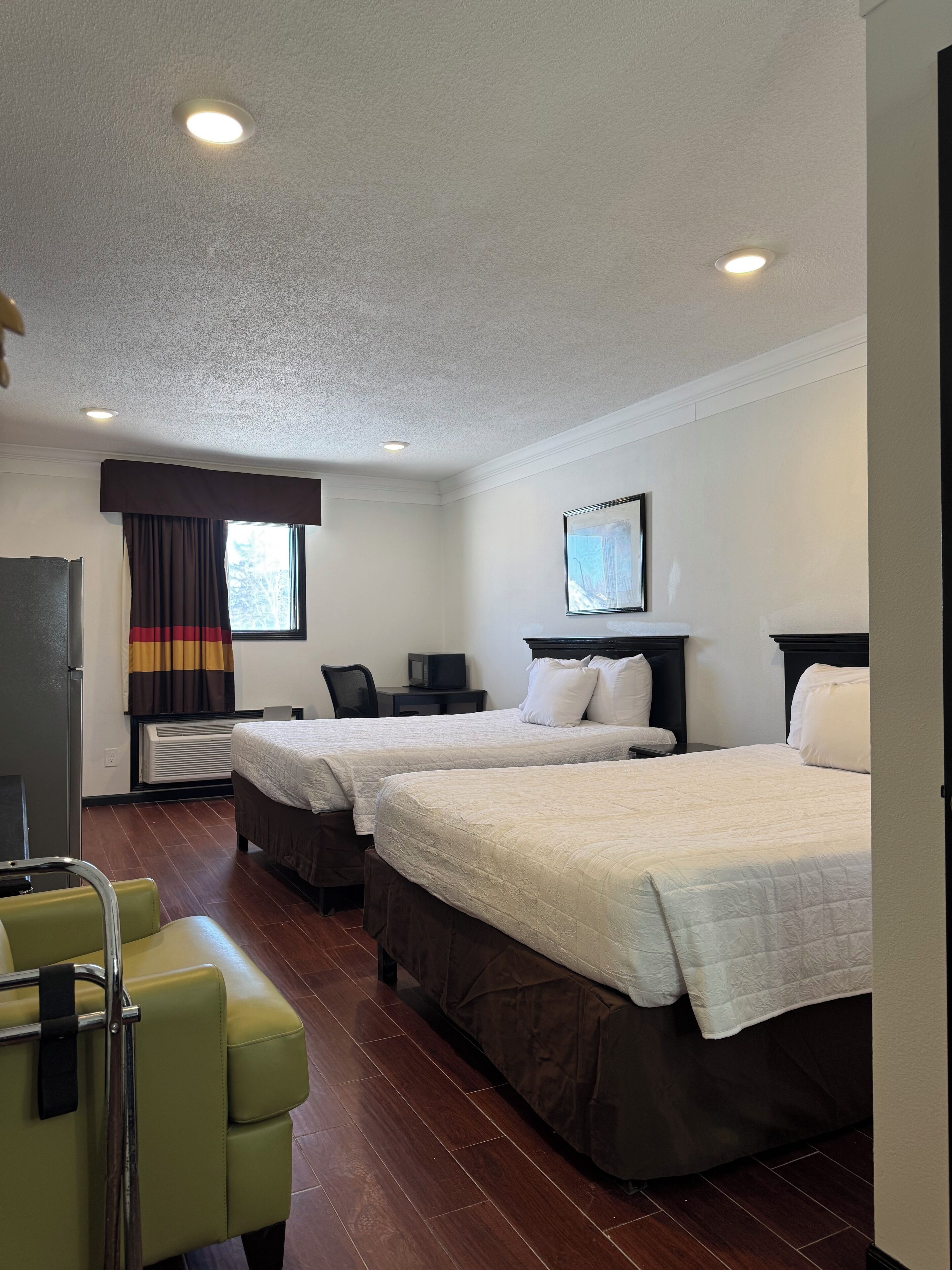 Una habitación de hotel con dos camas, un escritorio, una silla, una ventana con cortinas y un cuadro en la pared.