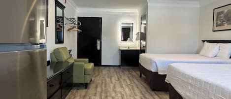 Une chambre d’hôtel compacte comprenant un coin cuisine, un lit simple, un petit espace salon et une salle de bain avec un miroir et un lavabo.