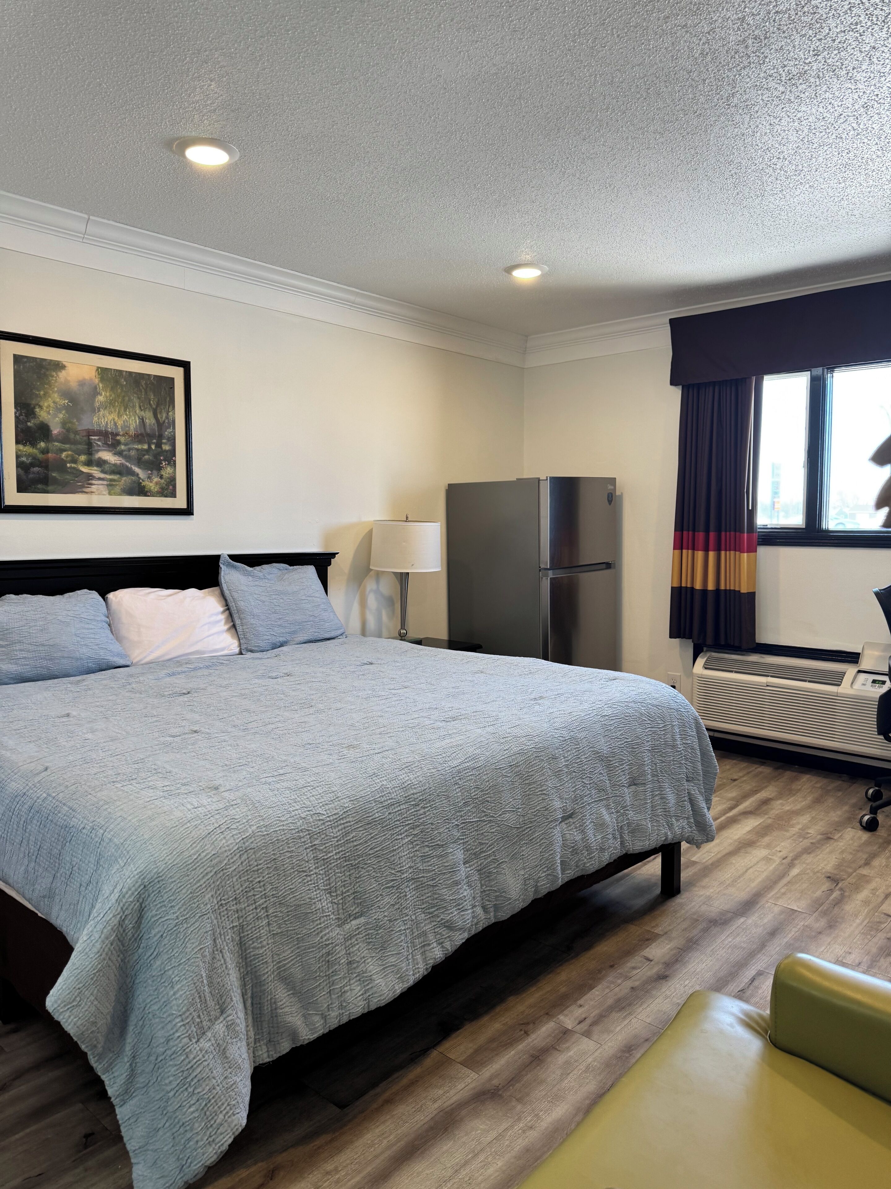 Une chambre d’hôtel avec un lit, un réfrigérateur, une lampe et une fenêtre avec des rideaux.