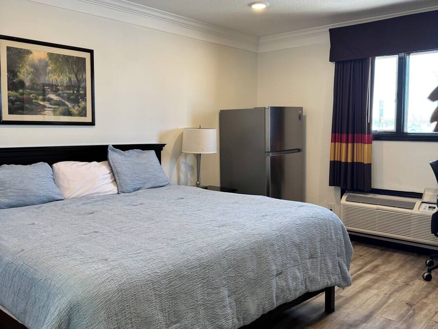 Une chambre d’hôtel avec un lit, un réfrigérateur, une lampe et une fenêtre avec des rideaux.