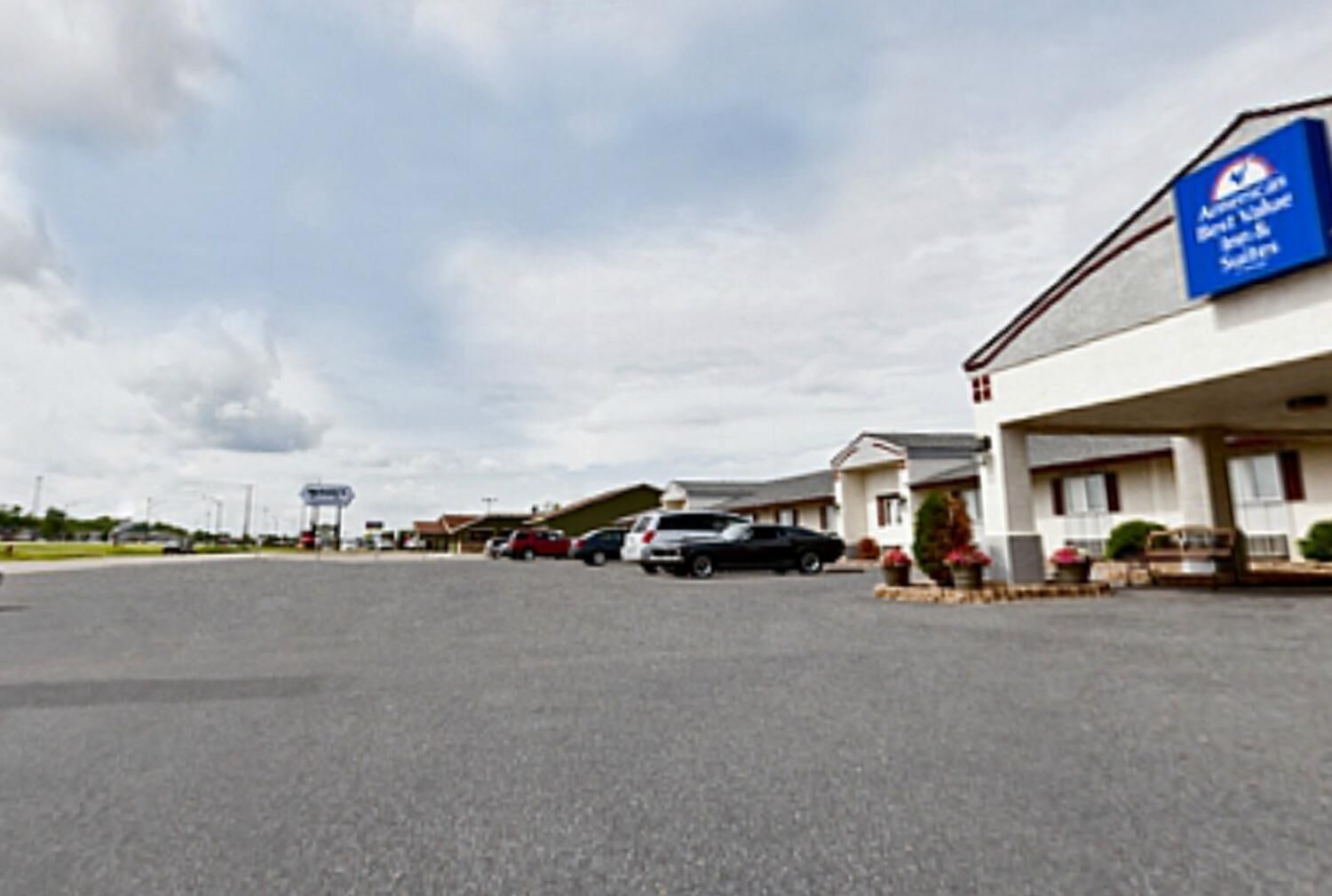 A motel with a blue sign, a parking lot, and several cars parked in front.