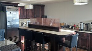Eine moderne Küche mit dunklen Holzschränken, einem Edelstahlkühlschrank, einer integrierten Kücheninsel mit Barhocker und einer Pendelleuchte.
