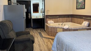 Ein Hotelzimmer mit Bett, Sofa, Schreibtisch, Kühlschrank und einem Badezimmer mit Badewanne. An der Wand hängt ein Bild.