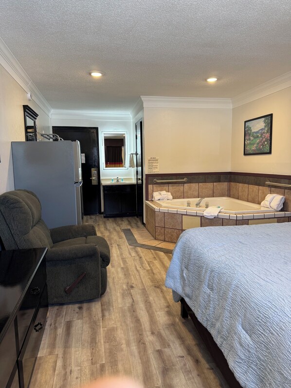 A hotel room with a bed, a sofa, a desk, a refrigerator, a bathroom with a bathtub, and a painting on the wall.