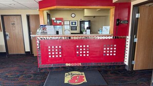 Un espace d’accueil avec un comptoir rouge, une horloge et le logo de Super 8 sur le tapis d’entrée.