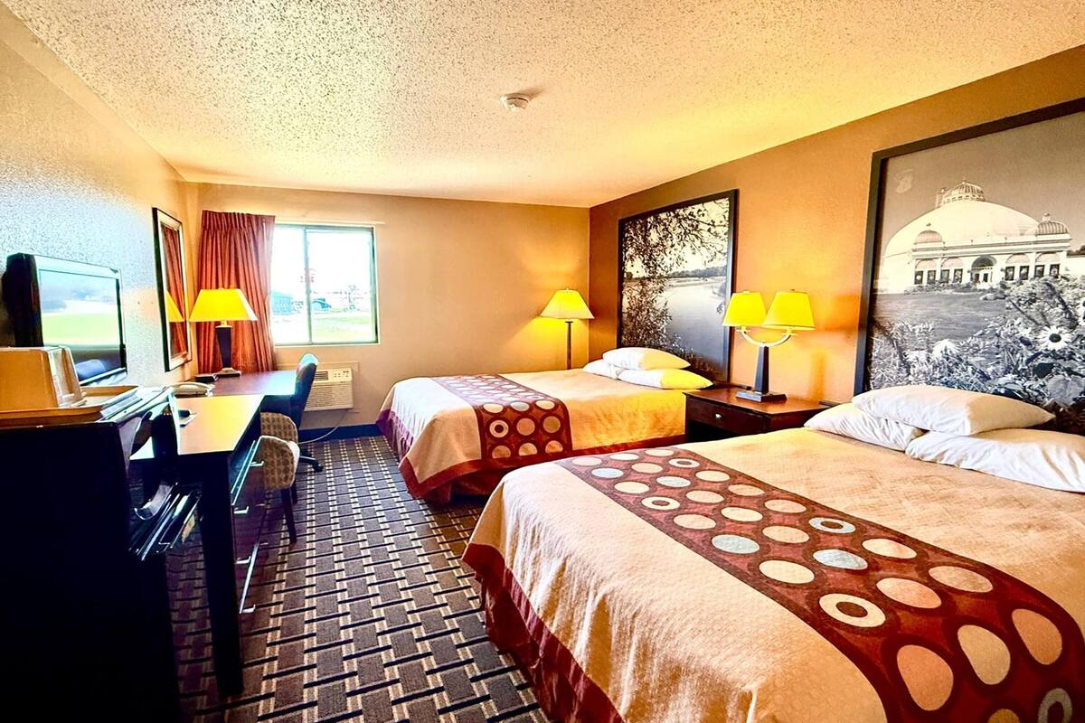 Une chambre d’hôtel avec deux lits, un bureau avec un ordinateur, une chaise, une télévision et une fenêtre avec des rideaux.
