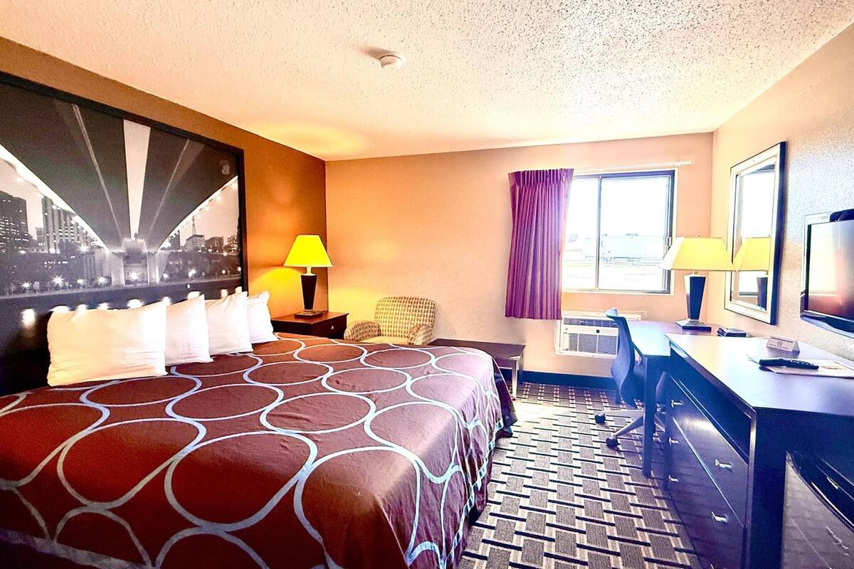 Une chambre d’hôtel avec un lit, un bureau, une chaise et une grande fenêtre avec des rideaux.