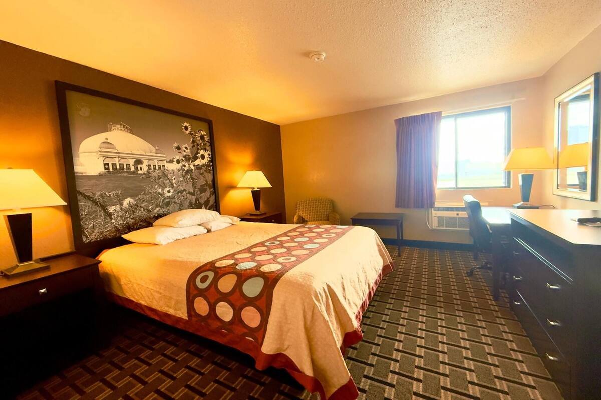 Une chambre d’hôtel avec un lit, deux lampes de chevet, un bureau, une chaise et une grande fenêtre avec des rideaux.