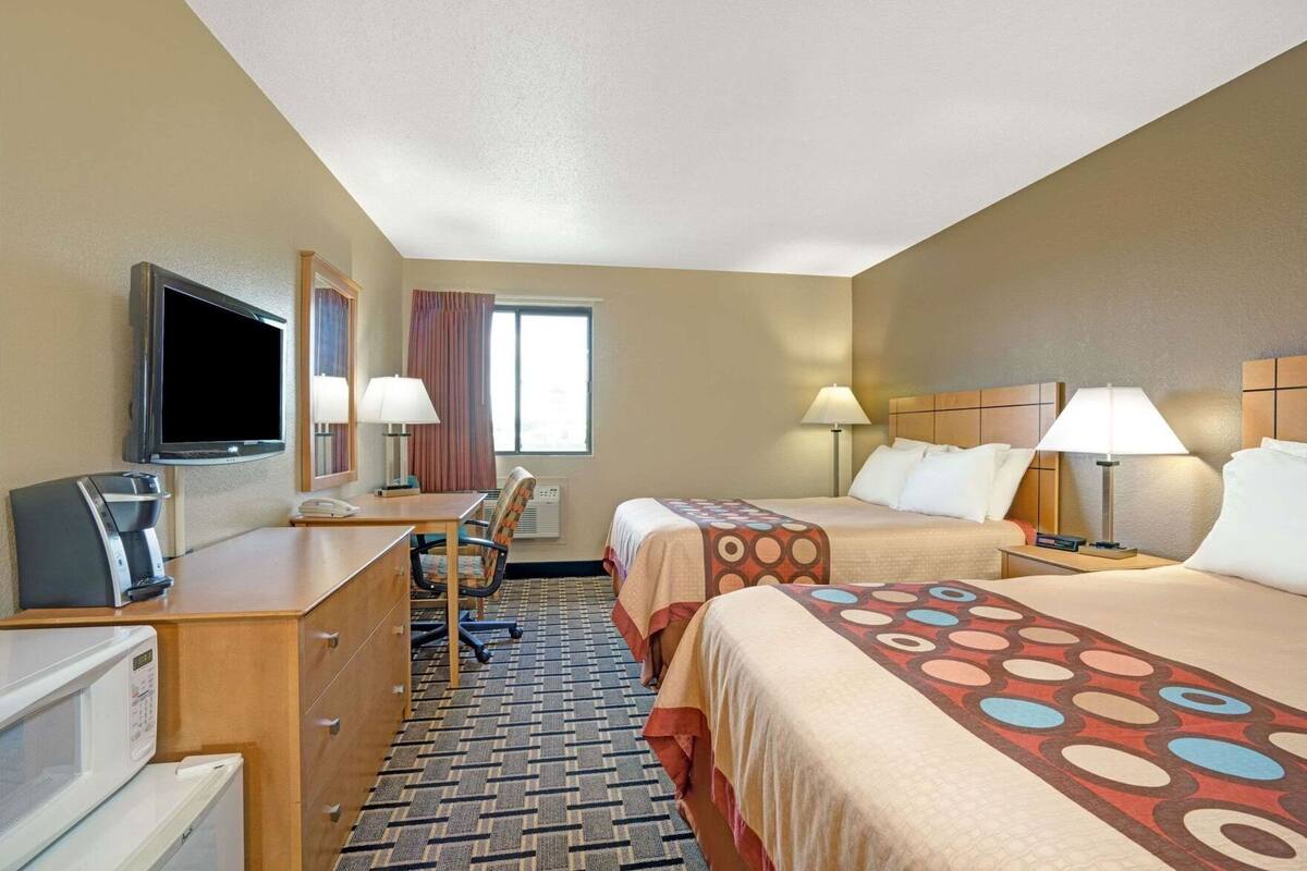 Une chambre d’hôtel avec deux lits, un bureau, une télévision, un four à micro-ondes et une fenêtre avec des rideaux.