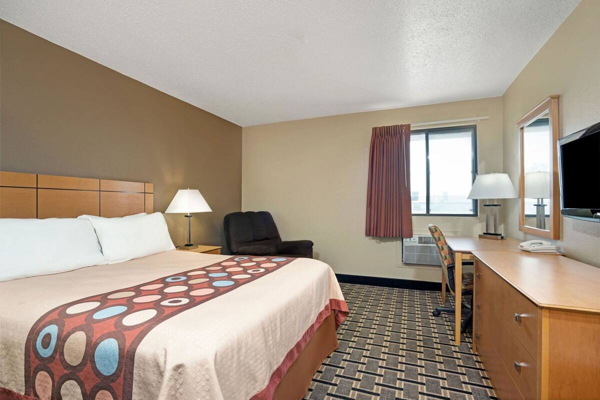 Une chambre d’hôtel équipée d’un lit, d’un bureau, d’une chaise, d’une télévision et d’une fenêtre avec des rideaux.