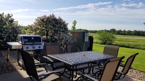 An outdoor patio with a grill, table, and chairs, surrounded by greenery and a clear sky. - Super 8 by Wyndham St. James (Saint James)