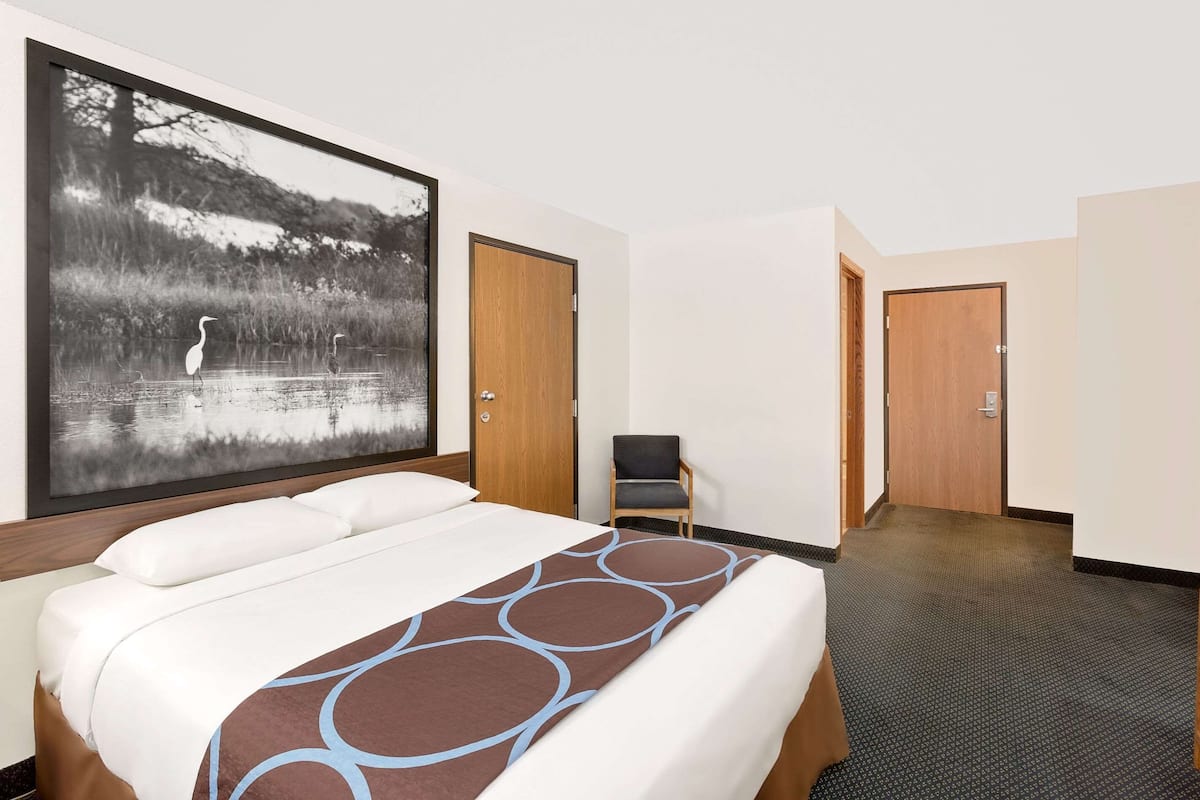 Una habitación de hotel con una cama grande, una silla y una puerta que da a otra estancia.