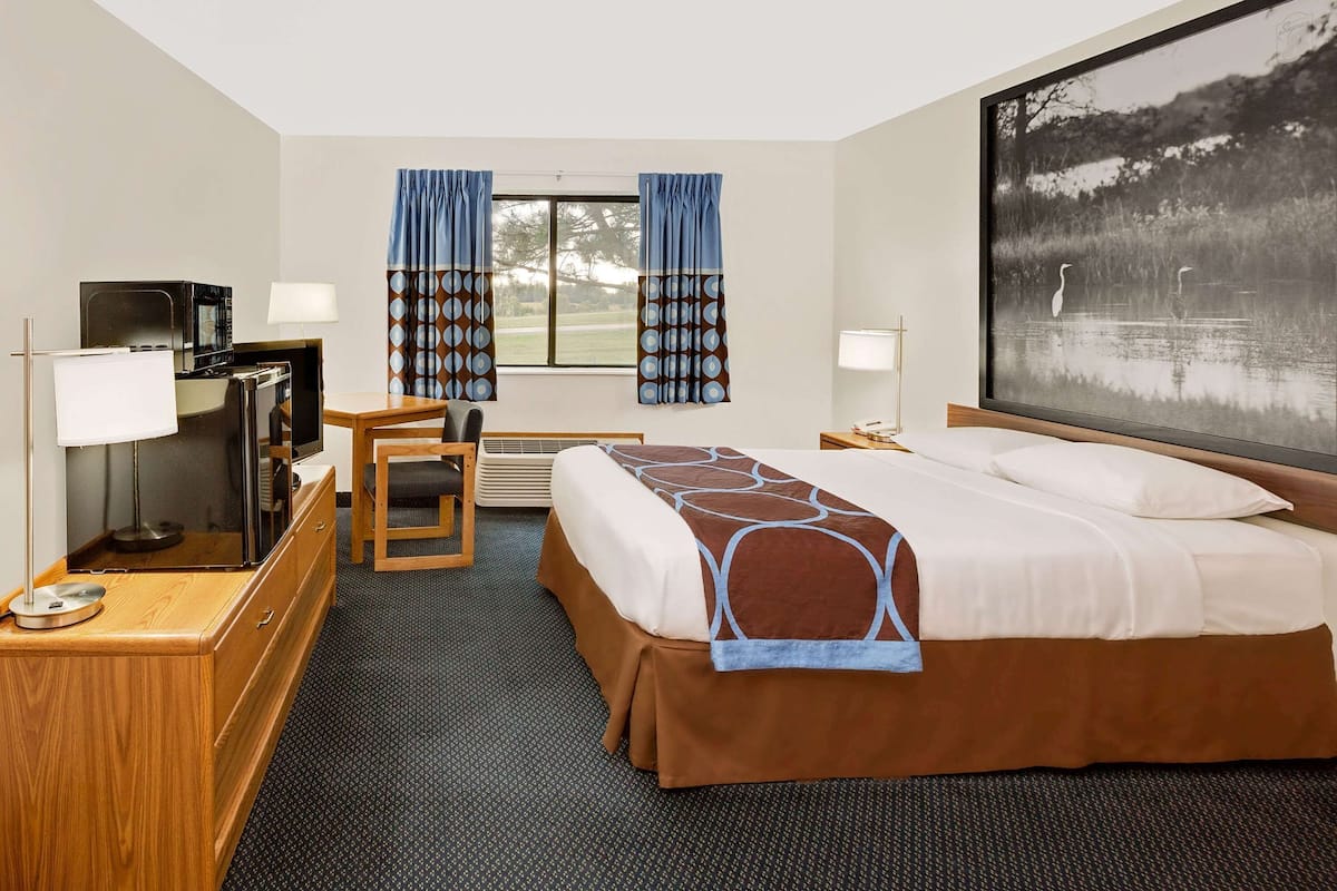 Habitación de hotel con cama, escritorio, silla, televisión y un amplio ventanal con cortinas.