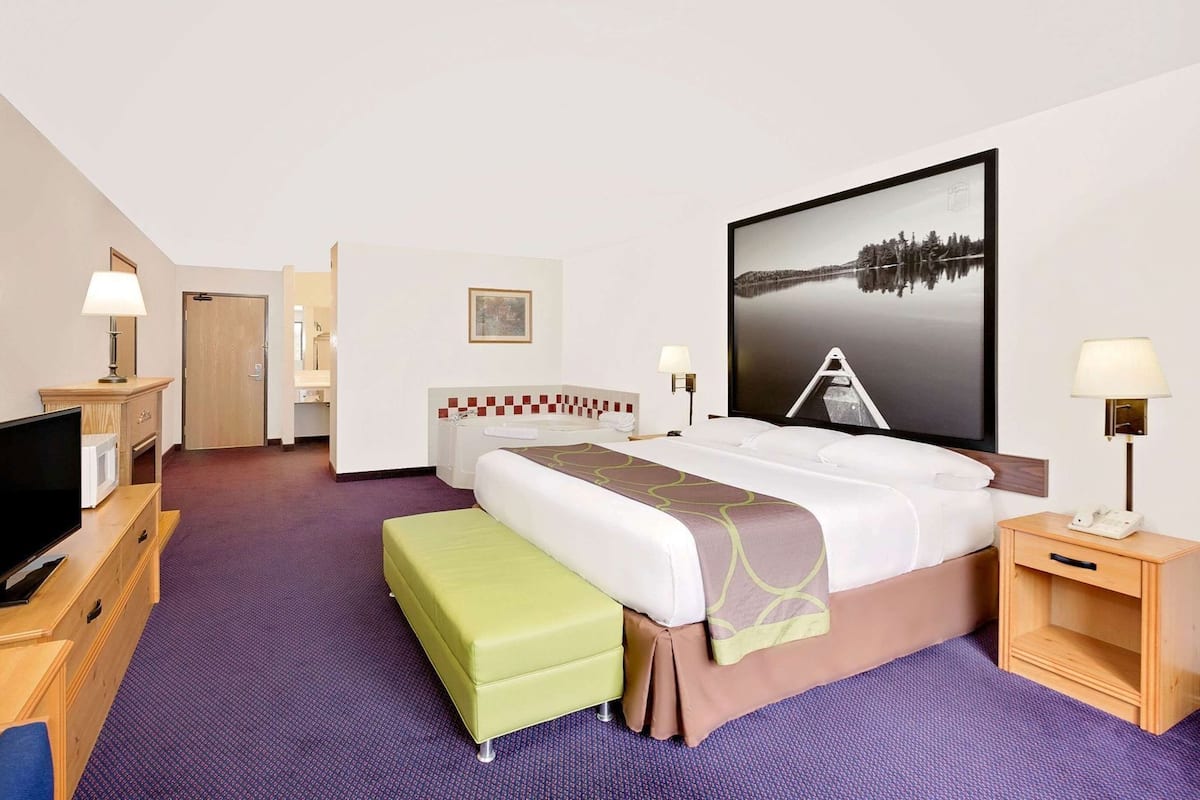 Habitación de hotel con cama, televisor, escritorio, silla, baño y un amplio ventanal.