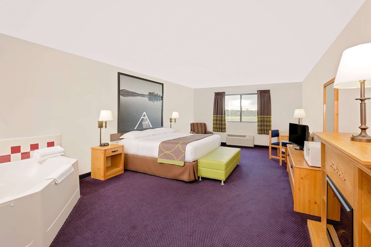Habitación de hotel con cama, escritorio, silla, televisor, lámpara y ventana con cortinas.