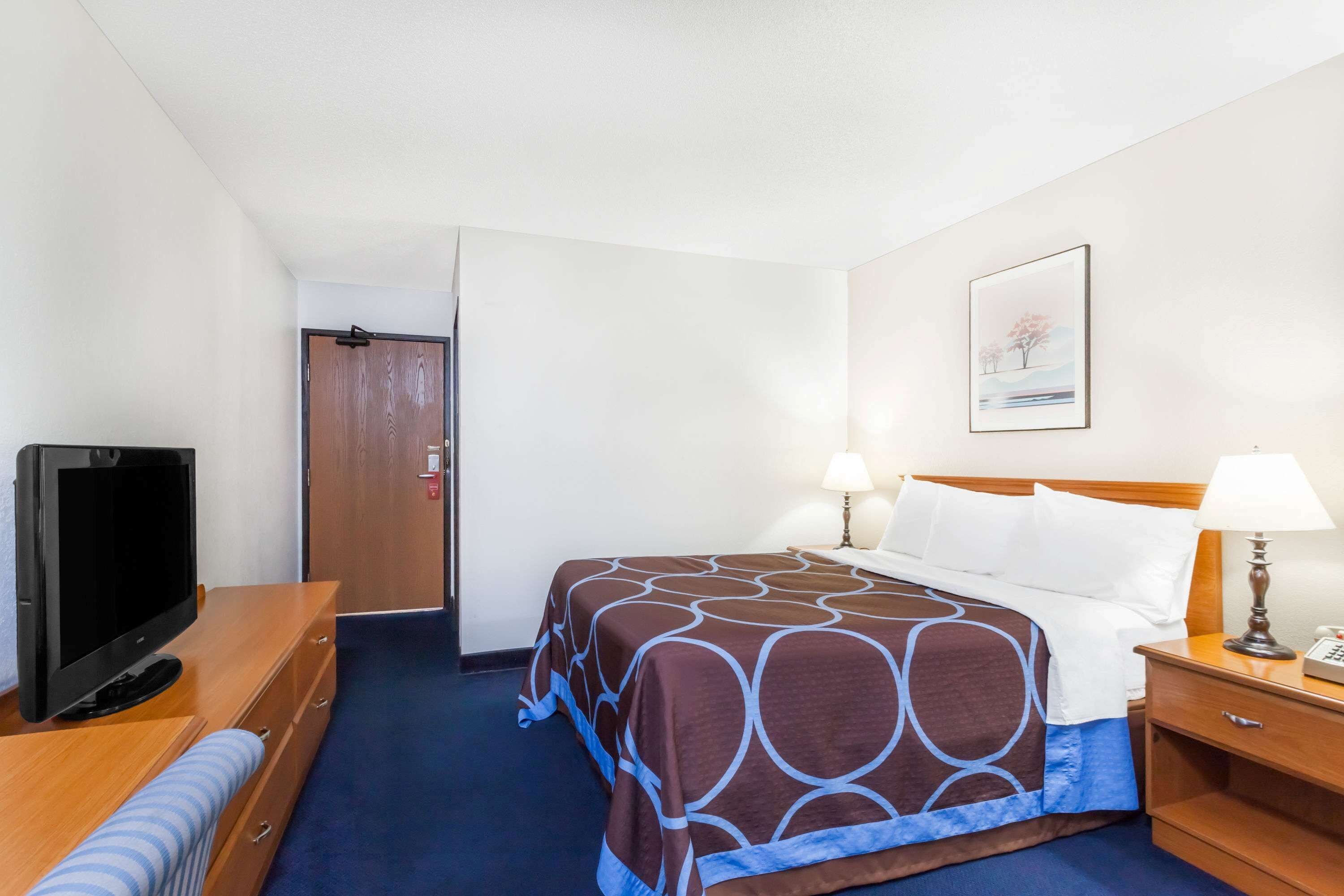 A hotel room with a bed, bedside lamps, a TV, and a wooden dresser.