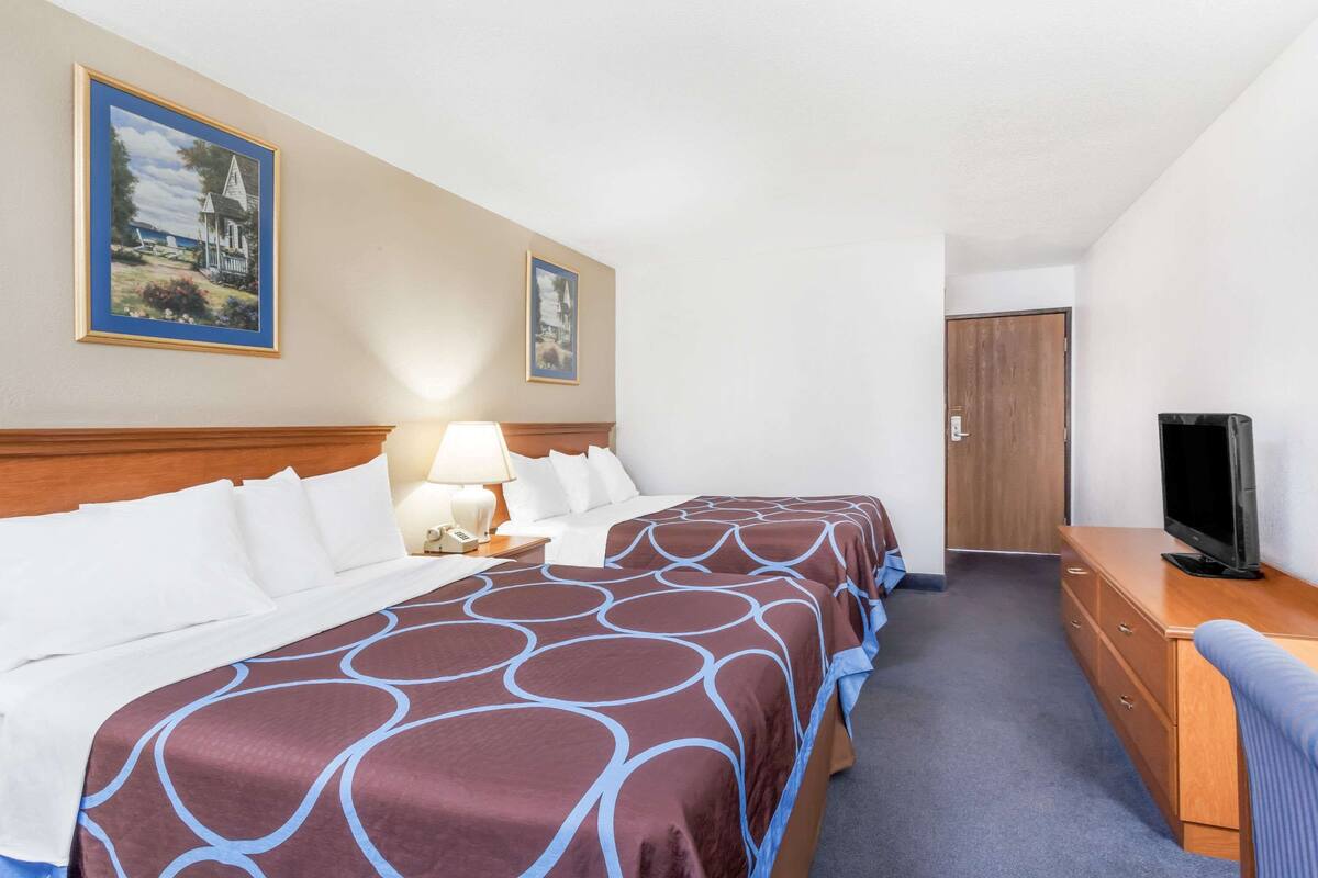 A hotel room with two beds, a TV, a desk, and a door.