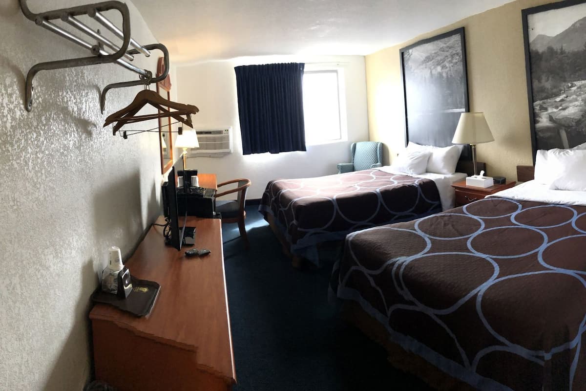 A hotel room with two beds, a desk, a chair, a lamp, and a window with curtains.