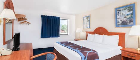 Habitación de hotel con cama, mesitas de noche, escritorio con teléfono, silla, televisor y ventana con cortinas.