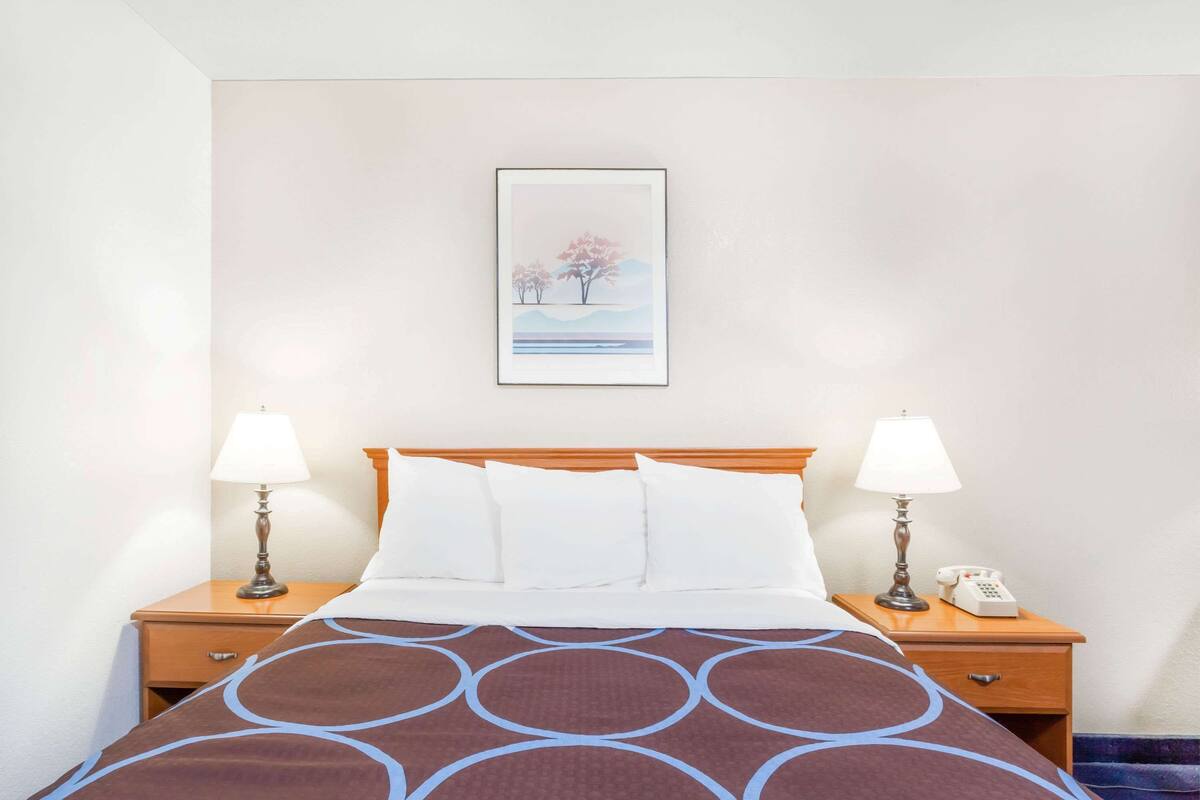 A hotel room with a bed, two bedside tables with lamps, a framed picture on the wall, and a telephone on one of the tables.