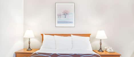 Une chambre d’hôtel avec un lit, deux tables de chevet avec des lampes, un tableau encadré au mur et un téléphone sur l’une des tables.