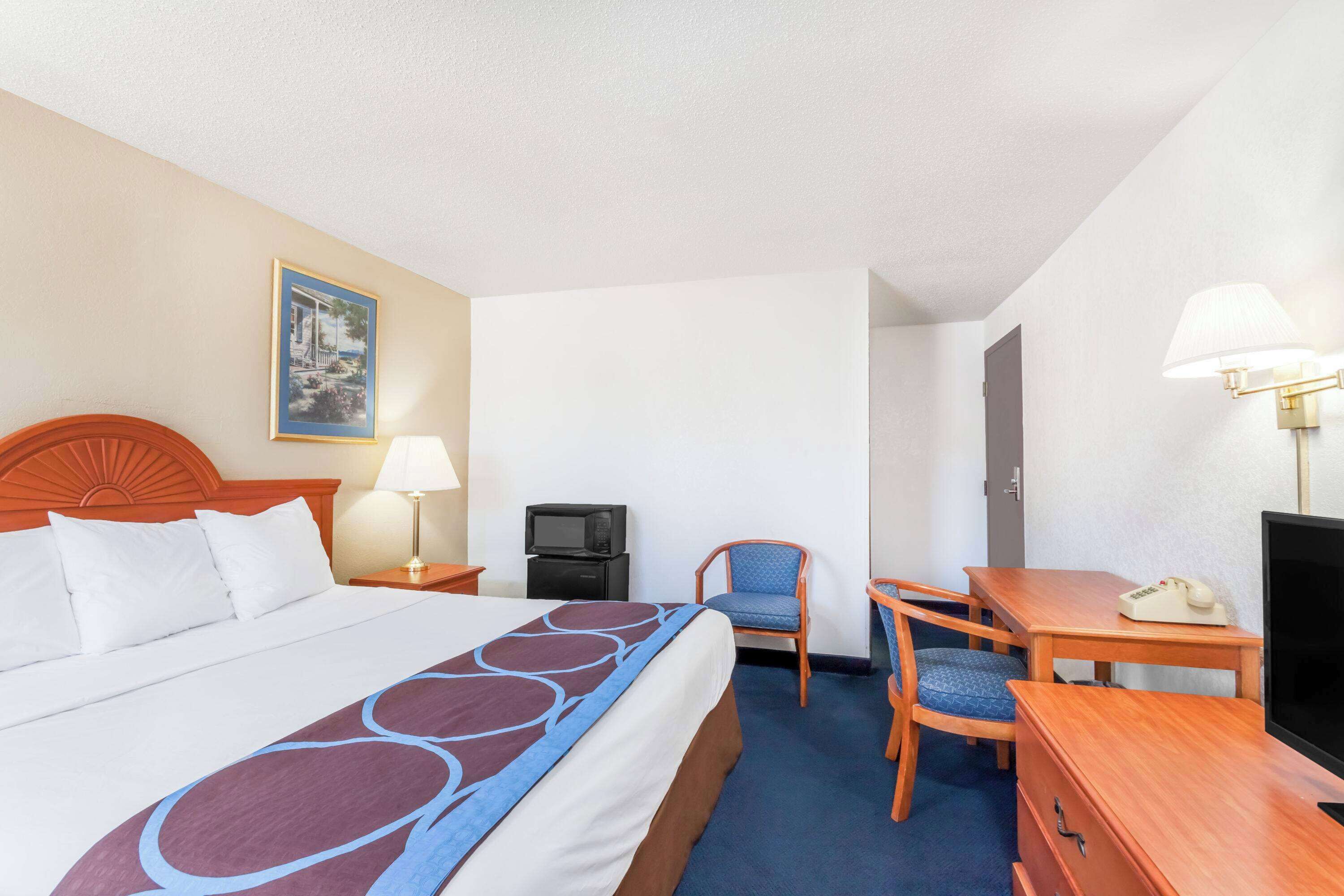 A hotel room with a large bed, a desk with a chair, a television, a lamp, and a telephone.