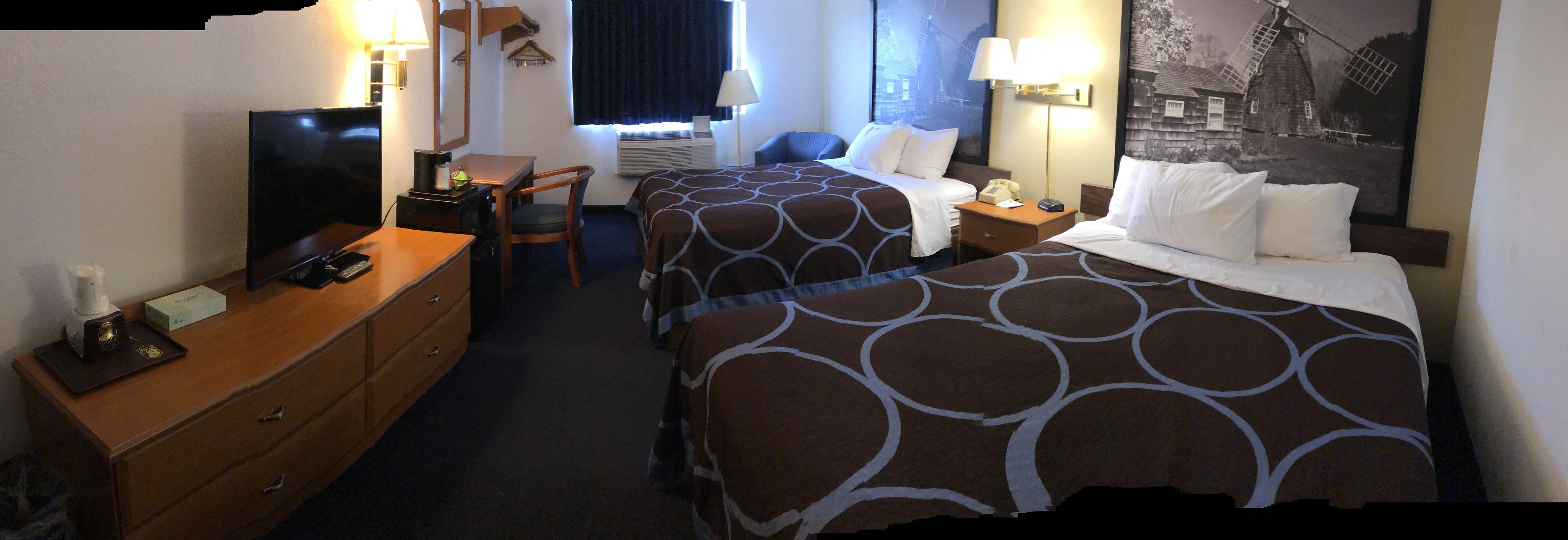 A hotel room with two beds, a desk with a television, a chair, and a large window with curtains.