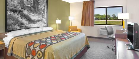 A hotel room with a large bed, two bedside lamps, a desk with a computer, and a large window with a view of greenery.