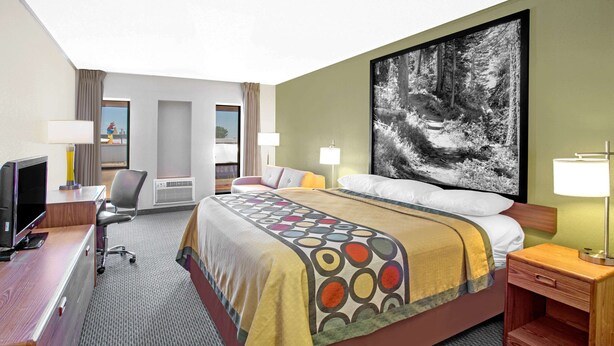 Una habitación de hotel con cama, escritorio, silla y un cuadro grande en la pared.