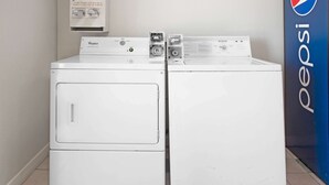 Un juego de lavadora y secadora Whirlpool en un cuarto de lavado con un cartel de Pepsi en la pared.