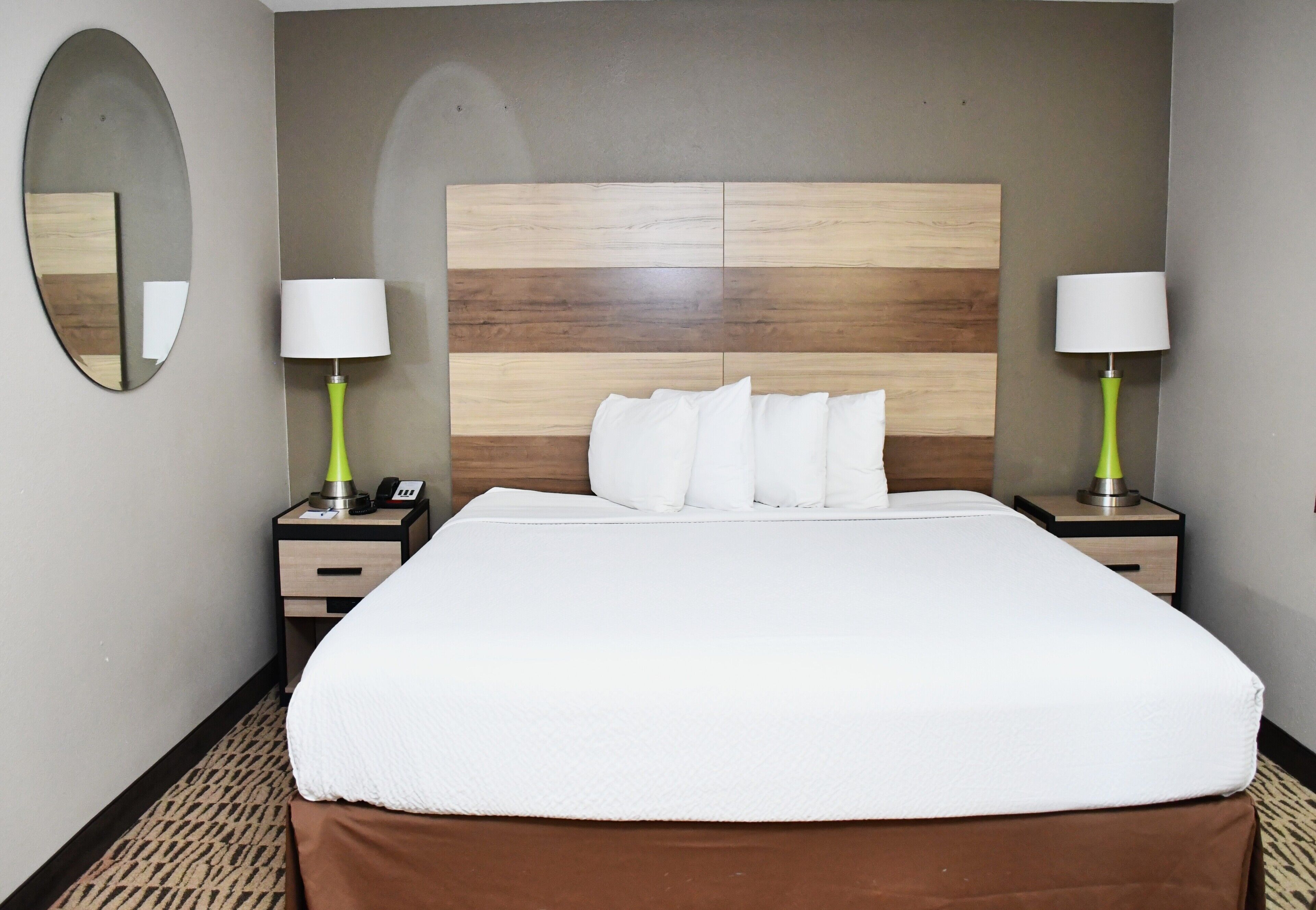 A hotel room with a large bed, two bedside tables with lamps, a mirror, and a wooden headboard.