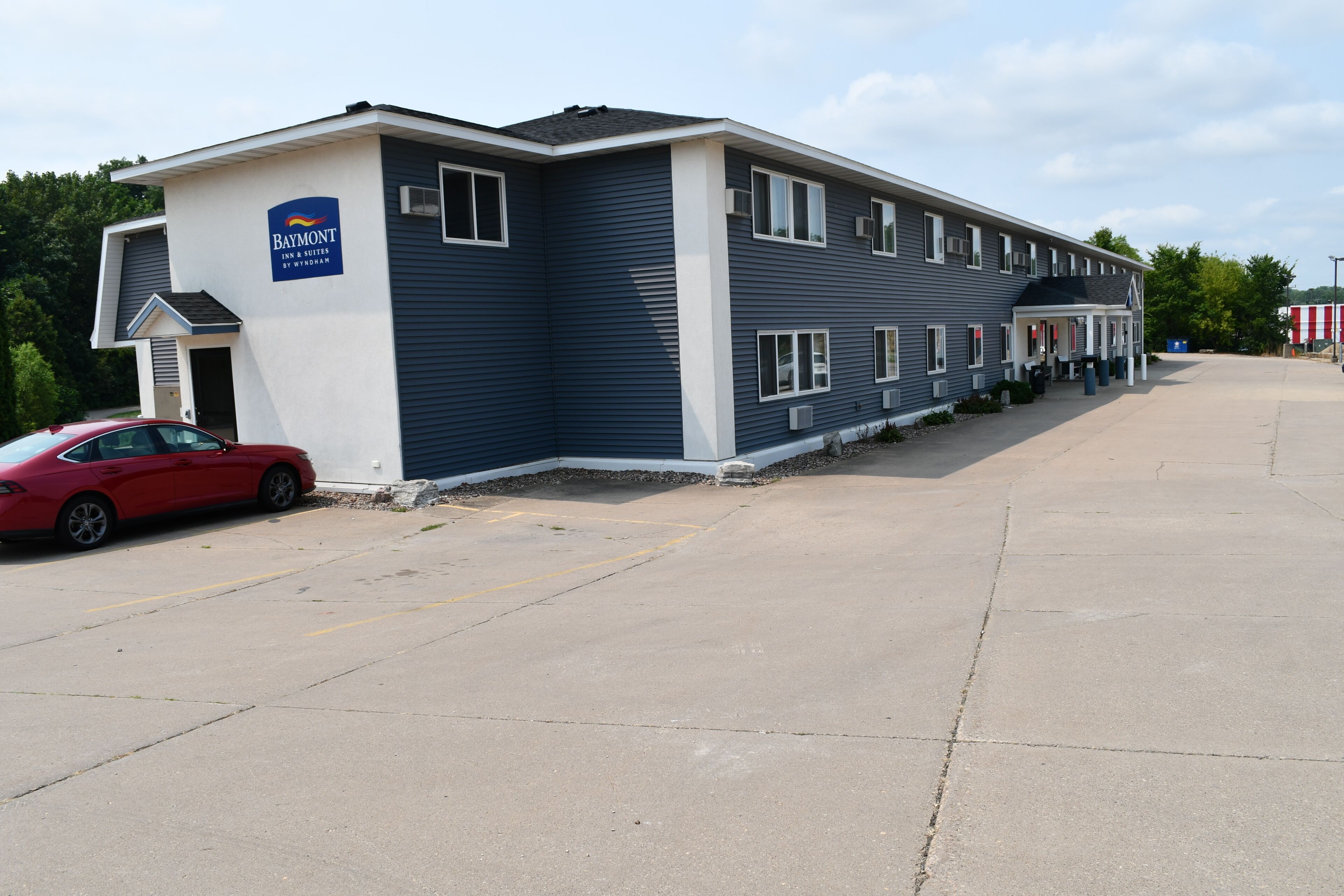 A Baymont Inn & Suites by Wyndham building with a parking lot and a red car parked in front.