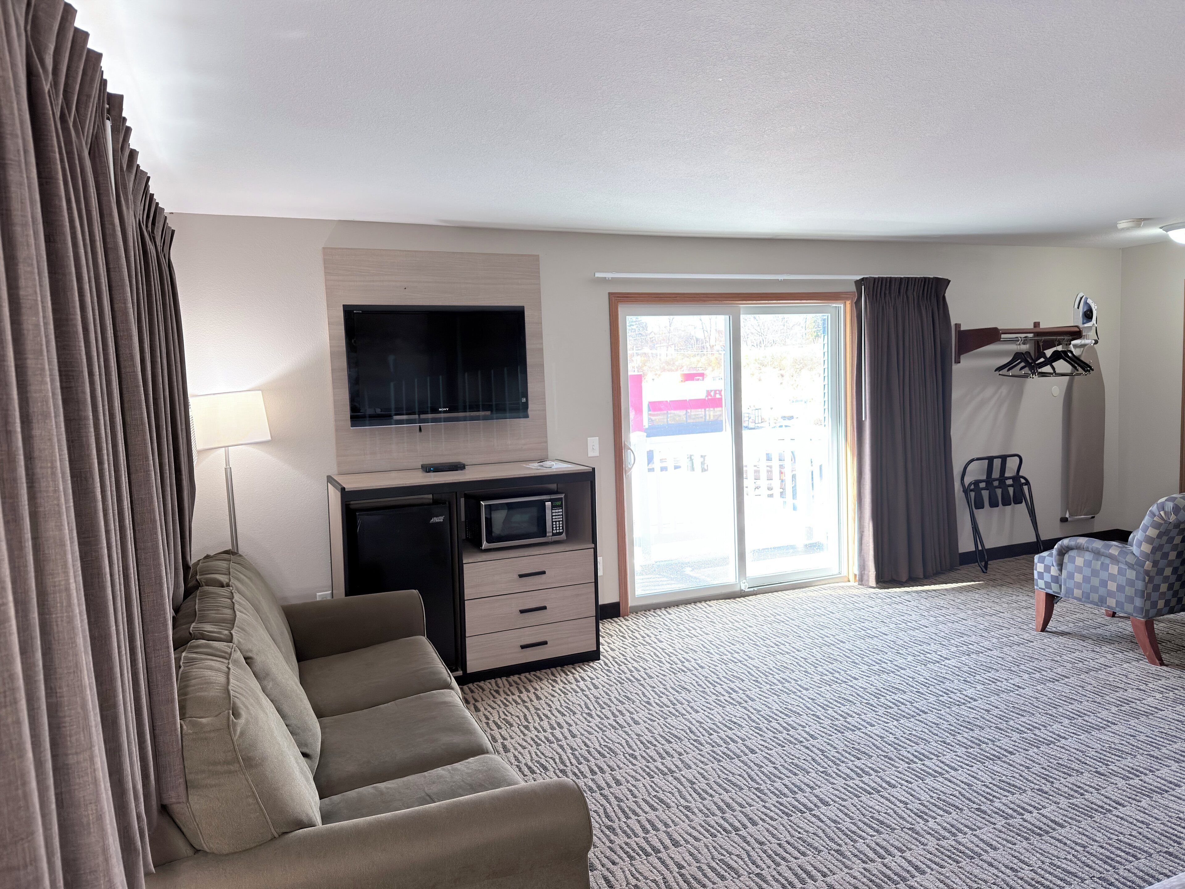 A hotel room with a sofa, a flat-screen TV, a microwave, a desk, and a sliding glass door leading to a balcony.
