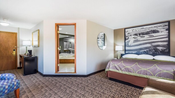 A hotel room with a bed, a desk, a chair, a mirror, and a door leading to a bathroom. -  Baymont Inn And Suites By Wyndham Platteville  (Platteville)