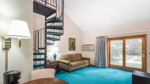 A room with a spiral staircase, a sofa, a coffee table, a lamp, and a large window. -  Baymont Inn And Suites By Wyndham Platteville  (Platteville)