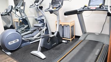 Un gimnasio con diverso equipo de ejercicio, incluyendo cintas de correr, bicicletas estáticas y una máquina de remo.