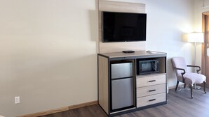 A modern hotel room with a flat-screen TV mounted on a wooden cabinet, a mini-fridge, a microwave, and a chair. -  Baymont Inn And Suites By Wyndham Platteville  (Platteville)
