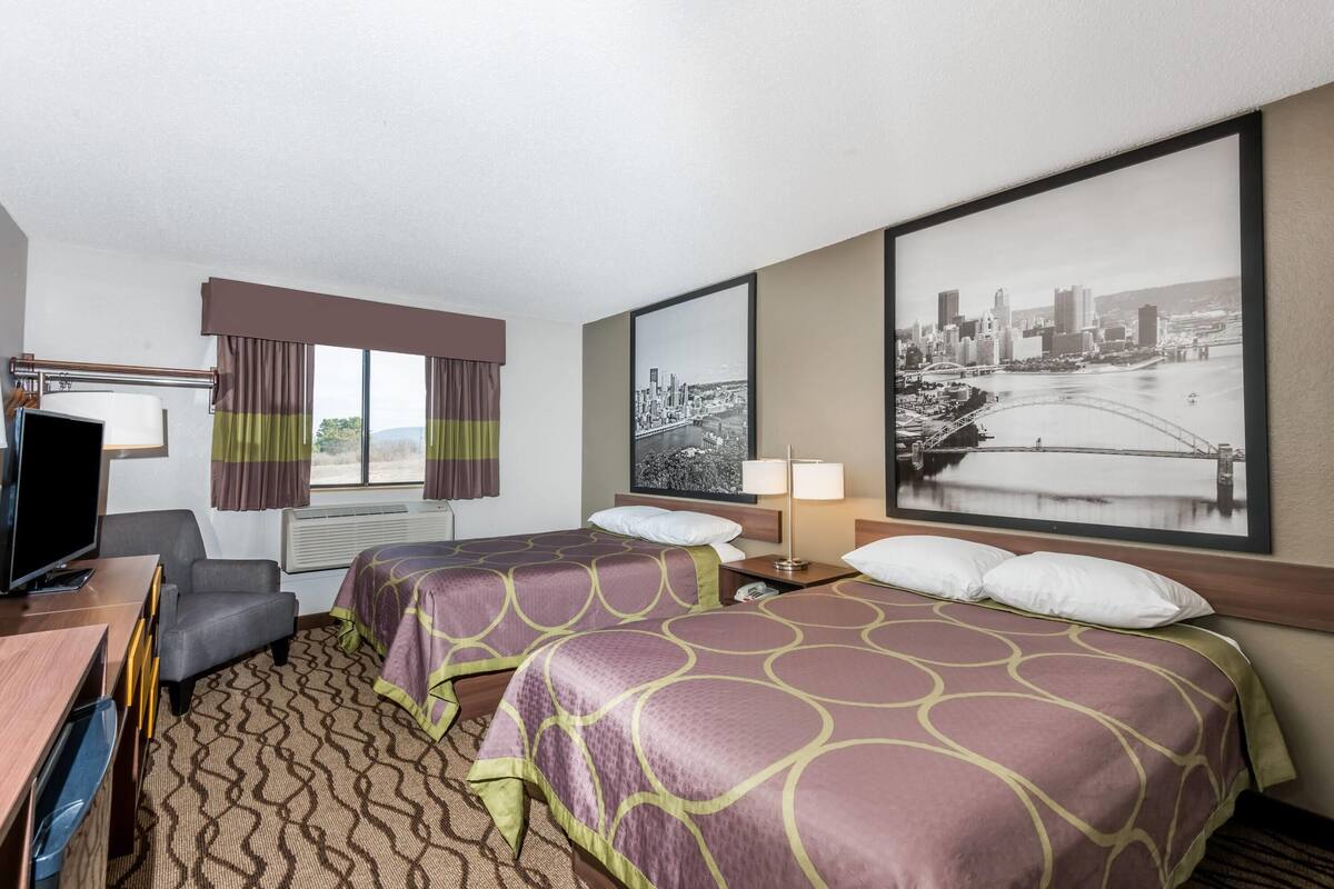 Une chambre d’hôtel avec deux lits, un bureau, une télévision, une fenêtre avec des rideaux et un tableau représentant un paysage urbain accroché au mur.
