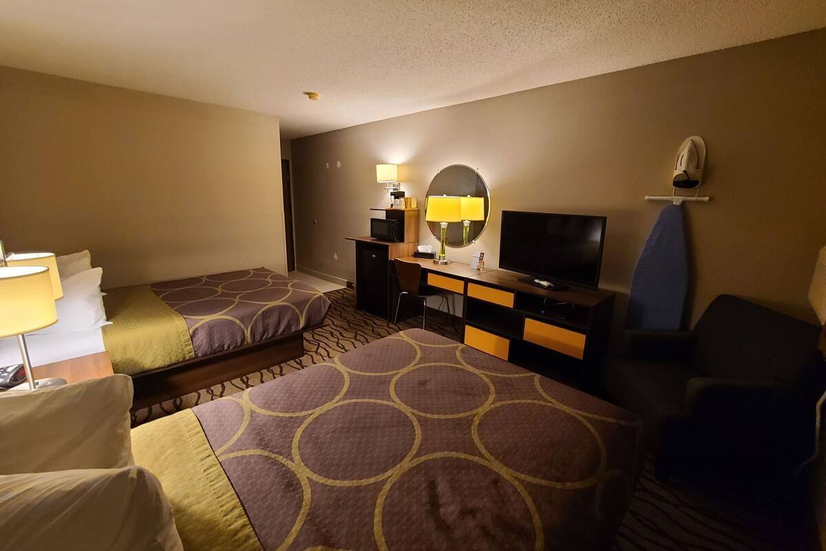 Une chambre d’hôtel avec deux lits, un bureau avec une télévision, un miroir et une chaise.