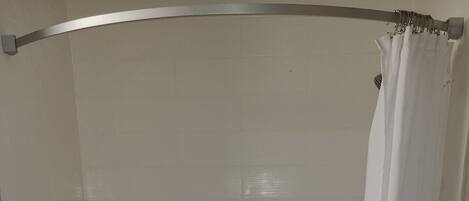 A walk-in shower with a white tiled wall, a grab bar, a small step stool, and a shower curtain.