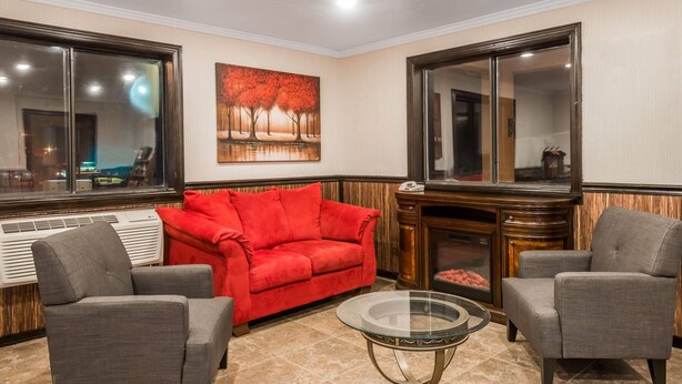 A living room with a red sofa, two grey armchairs, a glass coffee table, a fireplace, and a large mirror. - Super 8 by Wyndham Bedford (Bedford)